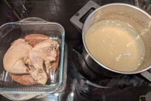Reserved cooked chicken pieces in a glass dish, next to the pot of broth in progress