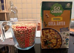 A box of dried whole Swedish yellow peas, next to a Pyrex measuring cup filled with peas