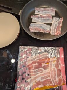 Raw bacon arranged ready to cook in a frying pan, with the rest laid out waiting on top of the package nearby