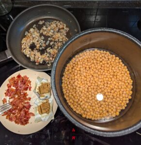 The Instant Pot inner pot with peas and cooking water, next to the crumbled bacon and the fried onion and garlic. Two bouillon cubes chopped into small pieces sit on their wrappers to one side of the bacon plate.