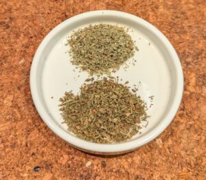 A small shallow ceramic dish with piles of dried savory and marjoram