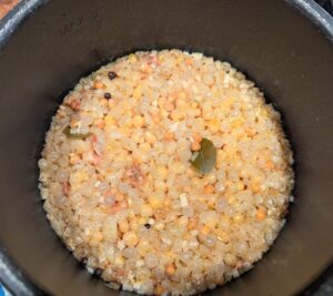A layer of loose pea skins, the bay leaves, and several allspice berries sit on top of the soup. A few undercooked peas were also pushed up by the floating skins. All of the cooking liquid is hidden underneath the layer of pea skins and spices.