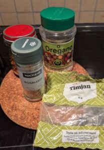 Containers of dried red chili flakes, rosematy, thyme, and oregano.
