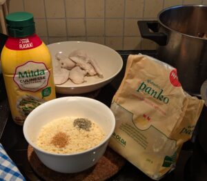A bowl with panko bread crumbs with seasonings visible on top sits between the open panko bag and a bottle of squeeze margarine.