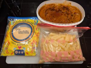 Clockwise: packaged corn tortillas, a plastic storage container of leftover chili con carne, and a zip bag of leftover cooked pasta for another recipe
