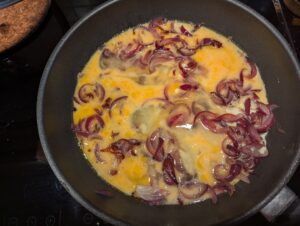 A pan with eggs and sautéed onions being scrambled together.