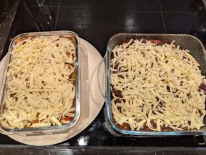 Two baking dishes side by side, both showing a generous layer of grated cheese just added on top.