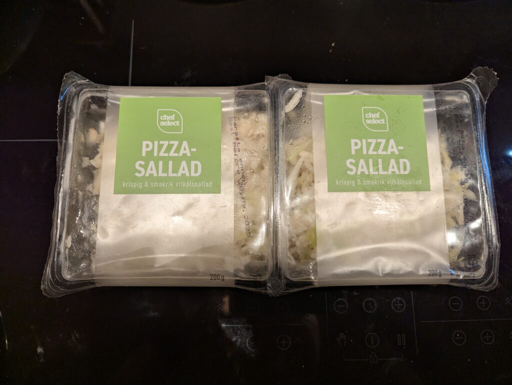 Two individual serving containers of a storebought oil and vinegar shredded cabbage salad.