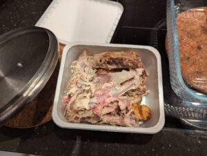 Half of a leftover roast chicken carcass, broken into smaller pieces and stored in a plastic refrigerator container
