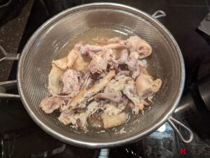 The boiled chicken carcass sitting in a mesh strainer on top of another pot