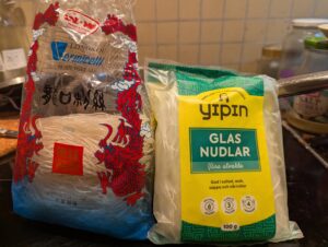 Two packages of bean thread noodles of different brands, one already open with two bundles remaining and the other package not yet opened