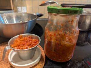 A small stainless measuring cup of kimchi stands next to the closed jar.