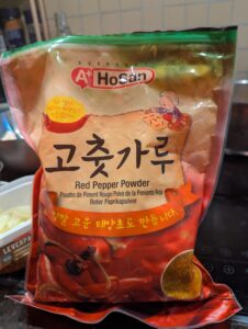A bag of HoSun brand gochugaru flakes, labeled "Red Pepper Powder" in English below the Korean text.