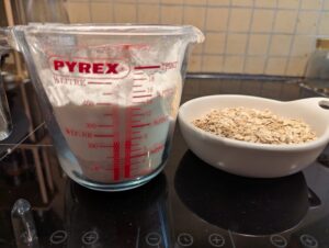 A British pint Pyrex measuring cup containing flours in two layers, with a bowl of rolled oats next to it.