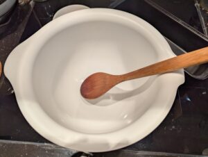 A white plastic mixing bowl with a big wooden spoon resting in it.