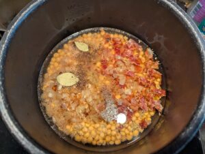 The soup pot with onions, bacon, and seasonings sitting on top of the peas before stirring them together.