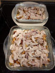 Two pans of stuffing mixture topped with chicken.