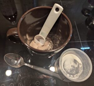 A brown ceramic coffee mug with yeast and a measuring spoon inside