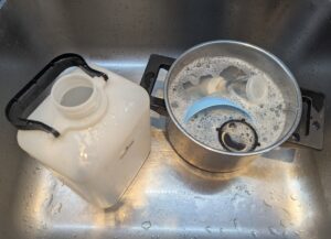 The sanitized fermentation jug sits open in a sink with the pot of sanitizing solution next to it