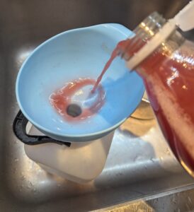 A bottle of juice being pured through a funnel into the jug