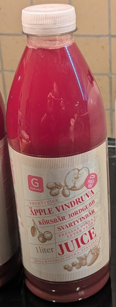 A plastic bottle labeled in large text as 'Garant Äpple Vindruva Körsbär Jordgubb Svartvinbär Juice'