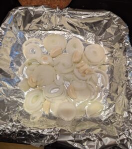 Sliced onions and whole garlic cloves in the bottom of a foil-lined baking dish.