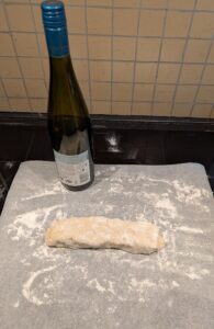 The dough shaped into a rectangle with a wine bottle for rolling in the background