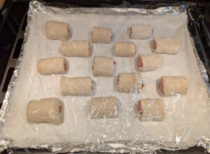 A baking sheet of uncooked rolls covered in plastic wrap