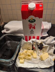 A liter capacity Pyrex pan sits next to a carton of milk and butter cut into smaller pieces on its paper wrapper