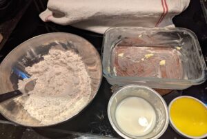 The bowl of combined dry ingredients next to the greased pan, the measured milk, and a small dish of melted butter.