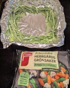 Frozen green beans arranged around the edges of a foil-lined baking pan, with an unopened bag of Herrgårds chunky vegetable mix in front of it