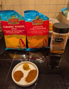 Packages of Kashmiri chili powder, turmeric, and paprika sit behind a small ceramic dish of measured spices