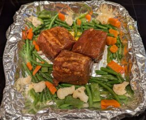 Pan of raw seasoned meat and veggies, with a temperature probe sticking out of the middle of one piece.