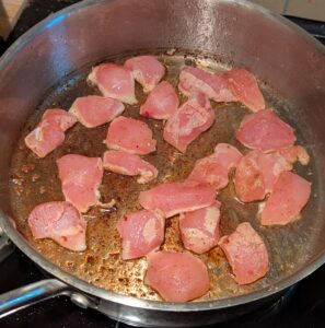 Raw chicken pieces spread out in the hot pan
