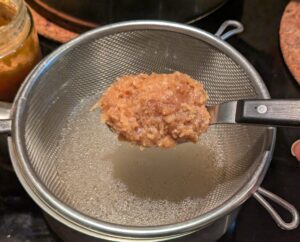 A spoonful of miso over a wire mesh strainer set into a small pan of broth