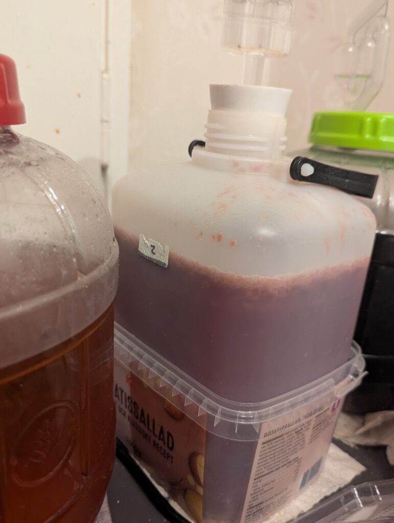 A fermentation jug of wine with a layer of fruit pulp and foam on top