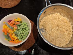 A bowl of mixed vegetables sits next to the rice pan.