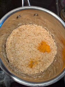 A pan of lightly sautéed rice with a measure of turmeric powder added on top