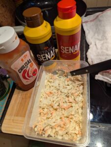 Sauces and coleslaw container sitting on a woodencutting board