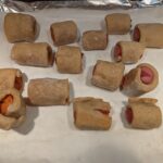 A larger shot of baked dough-wrapped sausages on a paper-covered baking tray