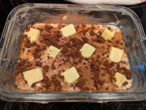 Batter in the pan topped with cinnamon and brown sugar, with cubes of butter arranged around the top