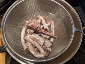 A strainer of bones sits over a pot of broth