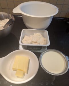 Leftover mashed potatoes sit with a cup of buttermilk, and a slab of butter on a dish prior to melting