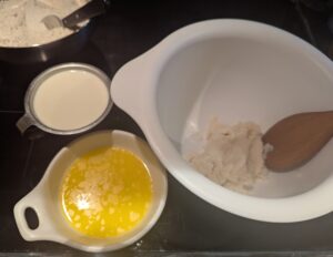 Potatoes in a mixing bowl with buttermilk and melted butter beside it