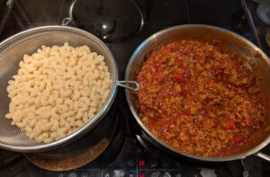 strainer of cooked macaroni sits next to a pan of meat sauce
