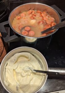 Small pan of sour cream and added starch, sitting in front of the soup pot with a ladle to transfer broth