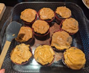 frosted cupcakes sitting in a Pyrex dish, with me holding the small spatula I used to distribute frosting over them