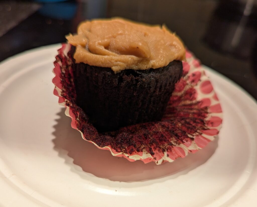 A half-peeled dark chocolate cupcake with peanut butter icing sits on a small white plate
