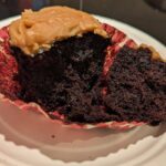 A very dark chocolate cupcake with peanut butter icing on top, broken open to show the crumb