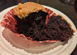 A very dark chocolate cupcake with peanut butter icing on top, broken open to show the crumb